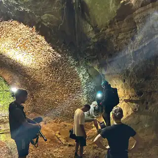 Sound recordist and crew inside the lit sandstone entrance chamber, with the gates and woodland light behind