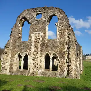 Ruins of an old stone building with arched windows on a grassy field, against a blue sky with some clouds.